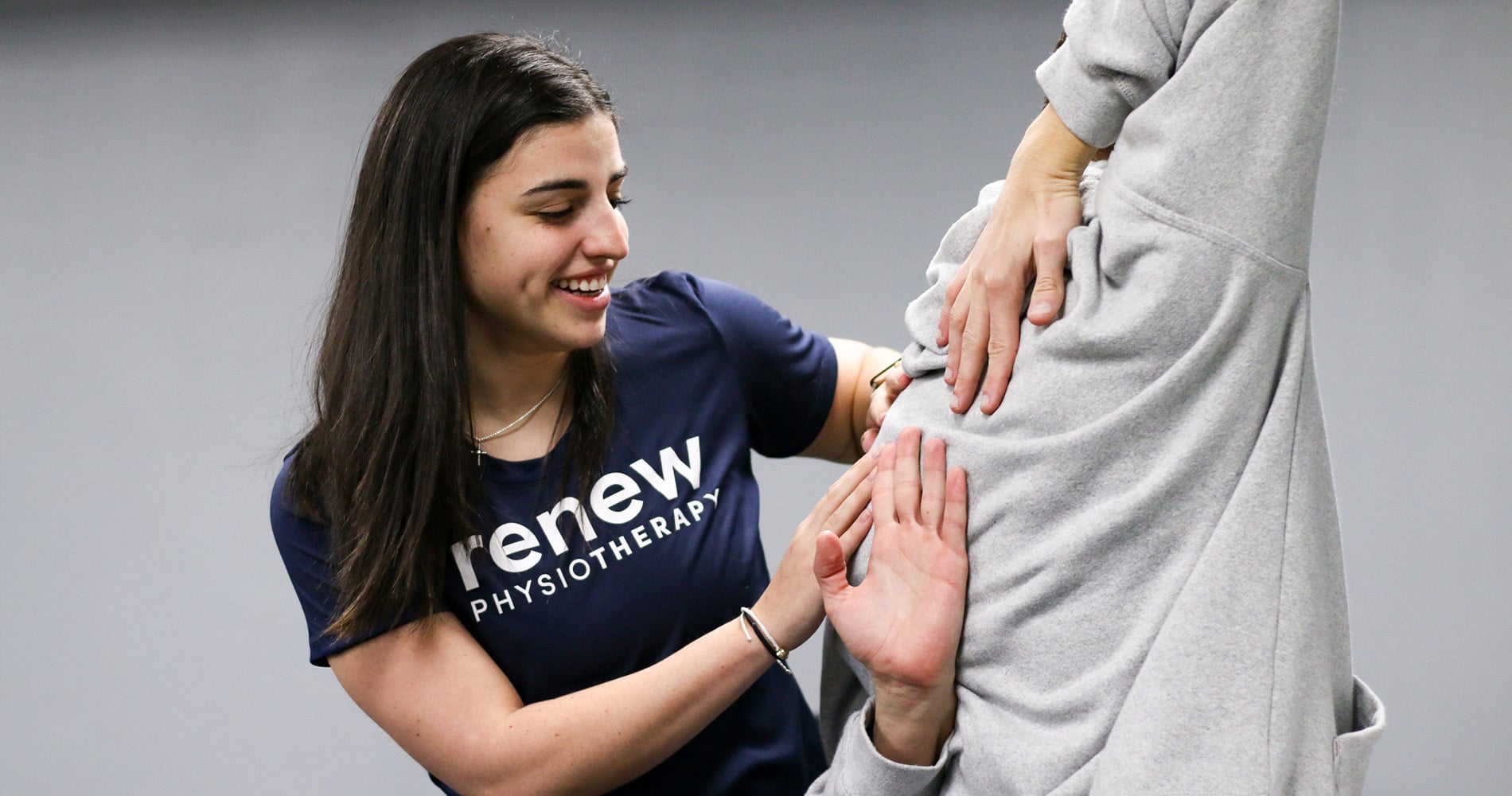 A Renew Wellness physiotherapist checks a patient’s lower back during a 1-on-1 physical therapy session.