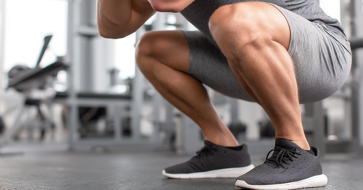 man perfoming a bodyweight squat in the gym in black shoes trying to get his knees over his toes 